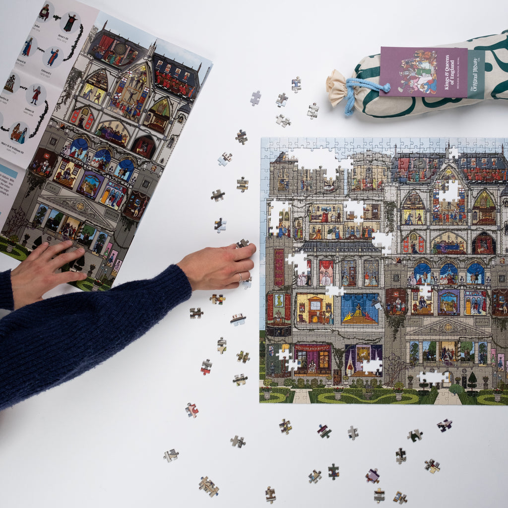 Person assembling a puzzle of a Royal Castle on a white surface with scattered pieces.